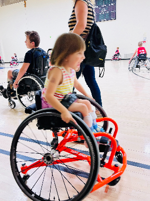 Theia zooming by during "shark and minnows" in the rascals 101 intro to wheelchair basketball class at Courage Kenny.